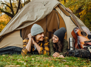 Young loved couple of tourists have a date in the forest. Attractive young woman and handsome man lying in the tent. Hugging lovers near campfire.
